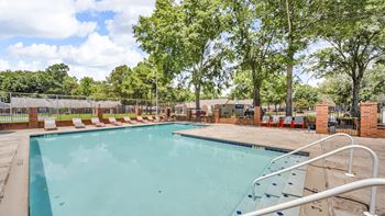 A large outdoor swimming pool surrounded by trees and lounge chairs.